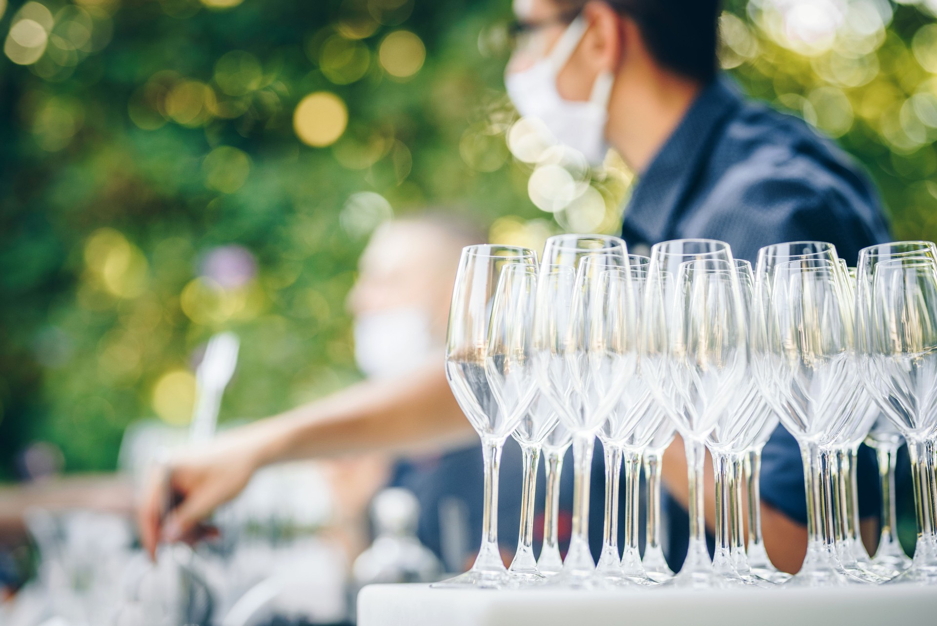 Outdoor catering bar service - a bartender with a protective face mask and champagne glasses in front of him. Outdoor party / event during coronavirus pandemic.